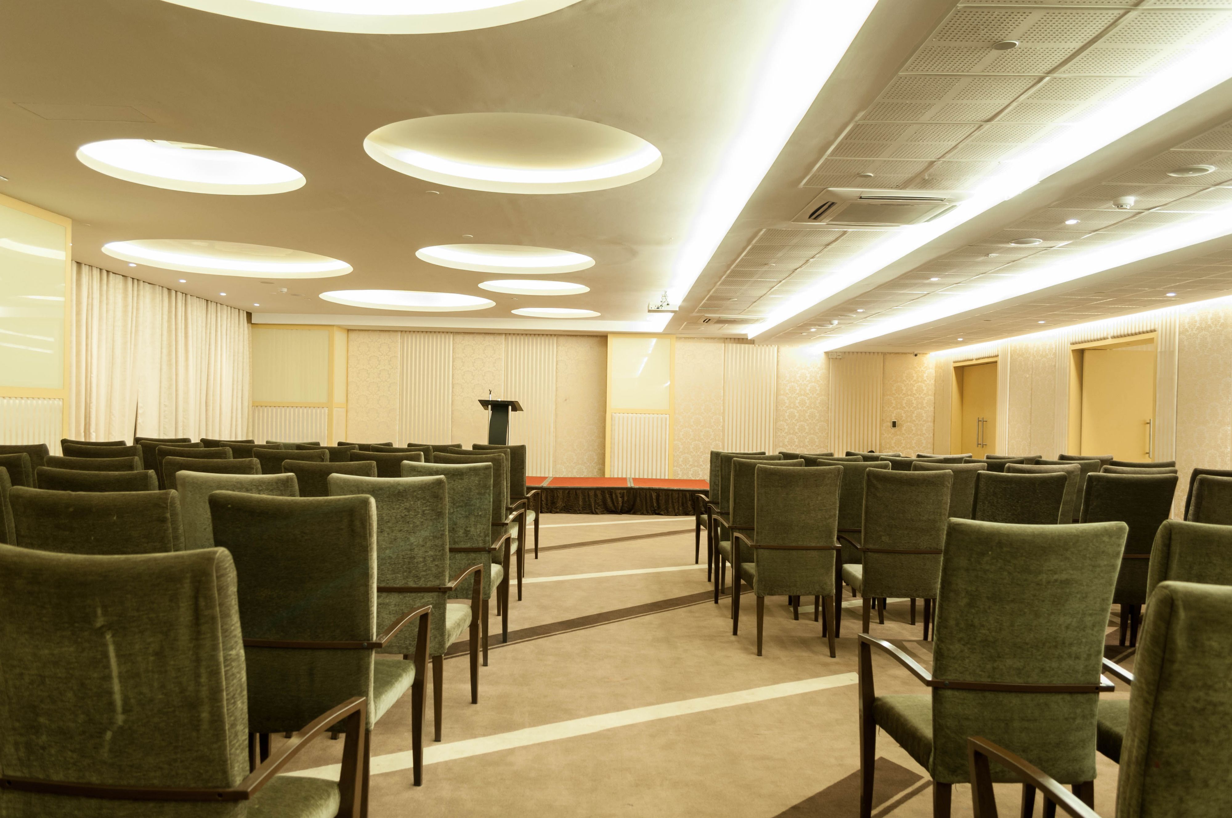 A conference room with rows of green chairs, a podium, and a carpeted floor.