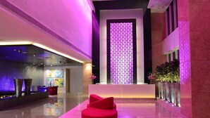 A modern lobby with a reception desk, a red seating area, and a decorative wall with a grid pattern. - E Hotel (Chennai)