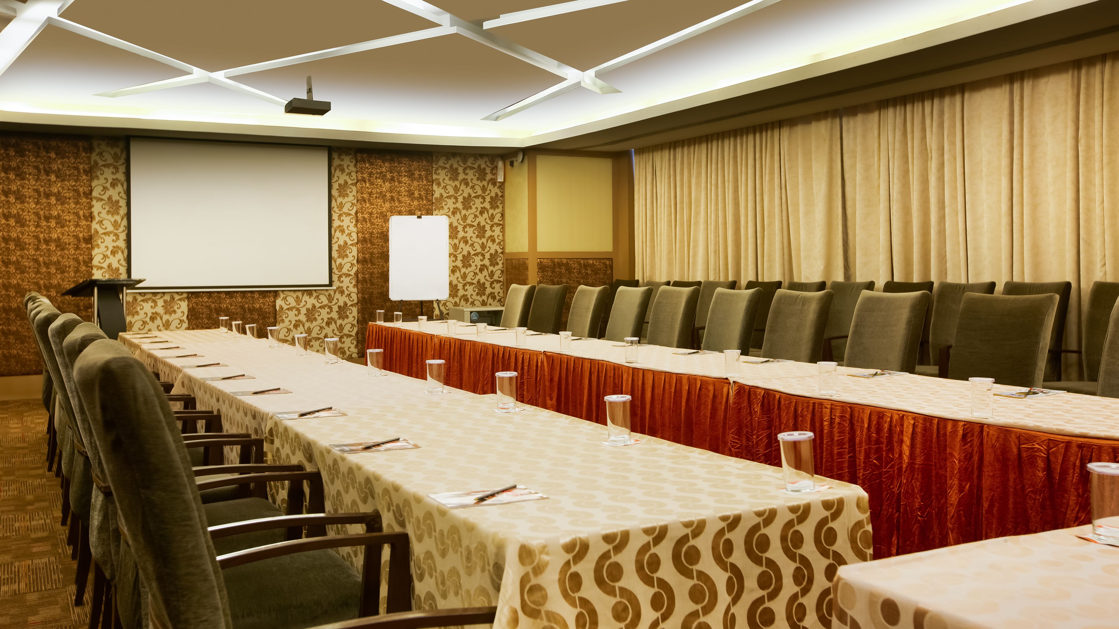 A conference room with a long table, chairs, a projector screen, and a whiteboard.