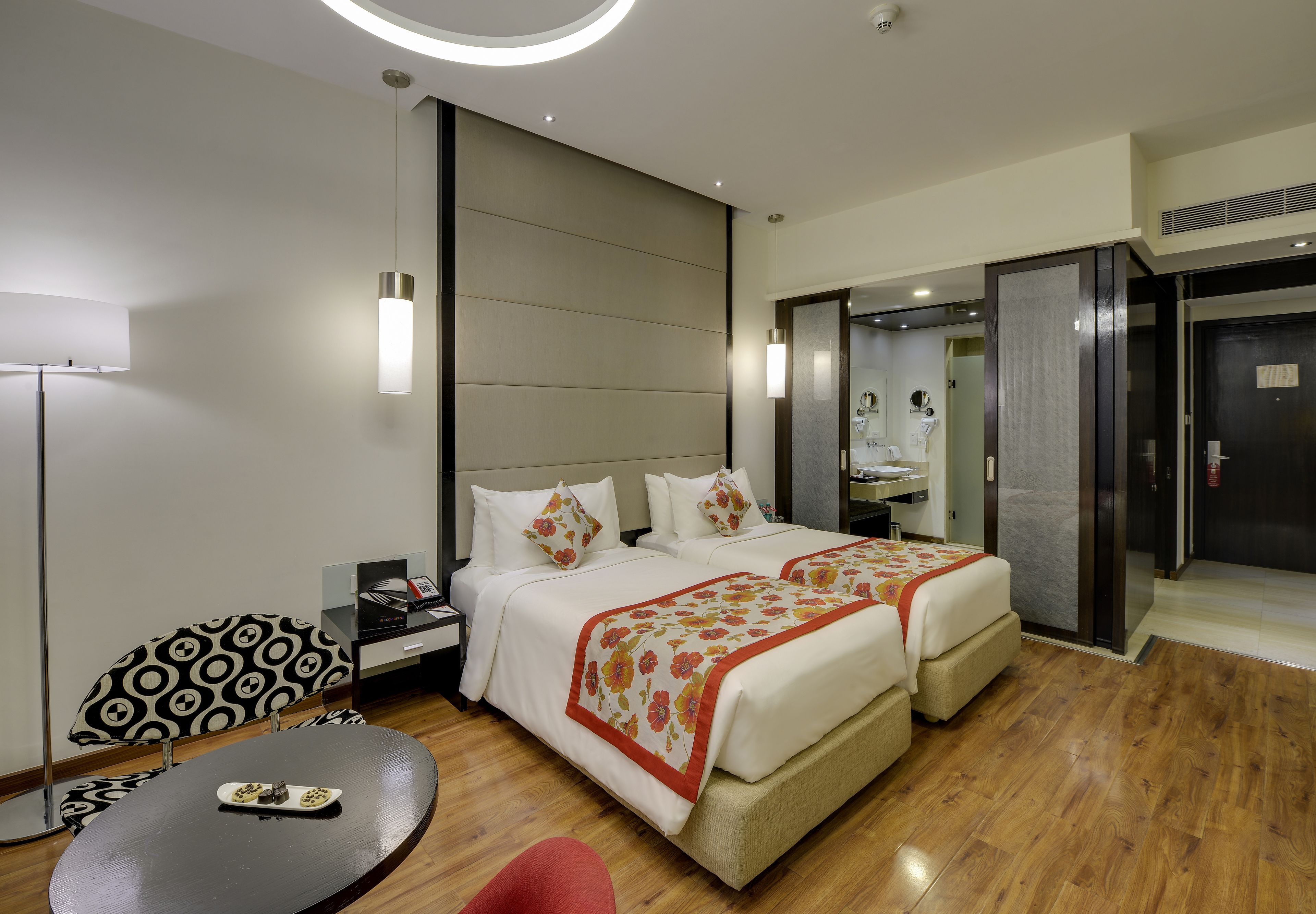 A hotel room with two beds, a desk, a chair, and a small table.