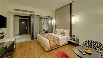 A hotel room with a bed, bedside table, chair, and a small table with fruit.