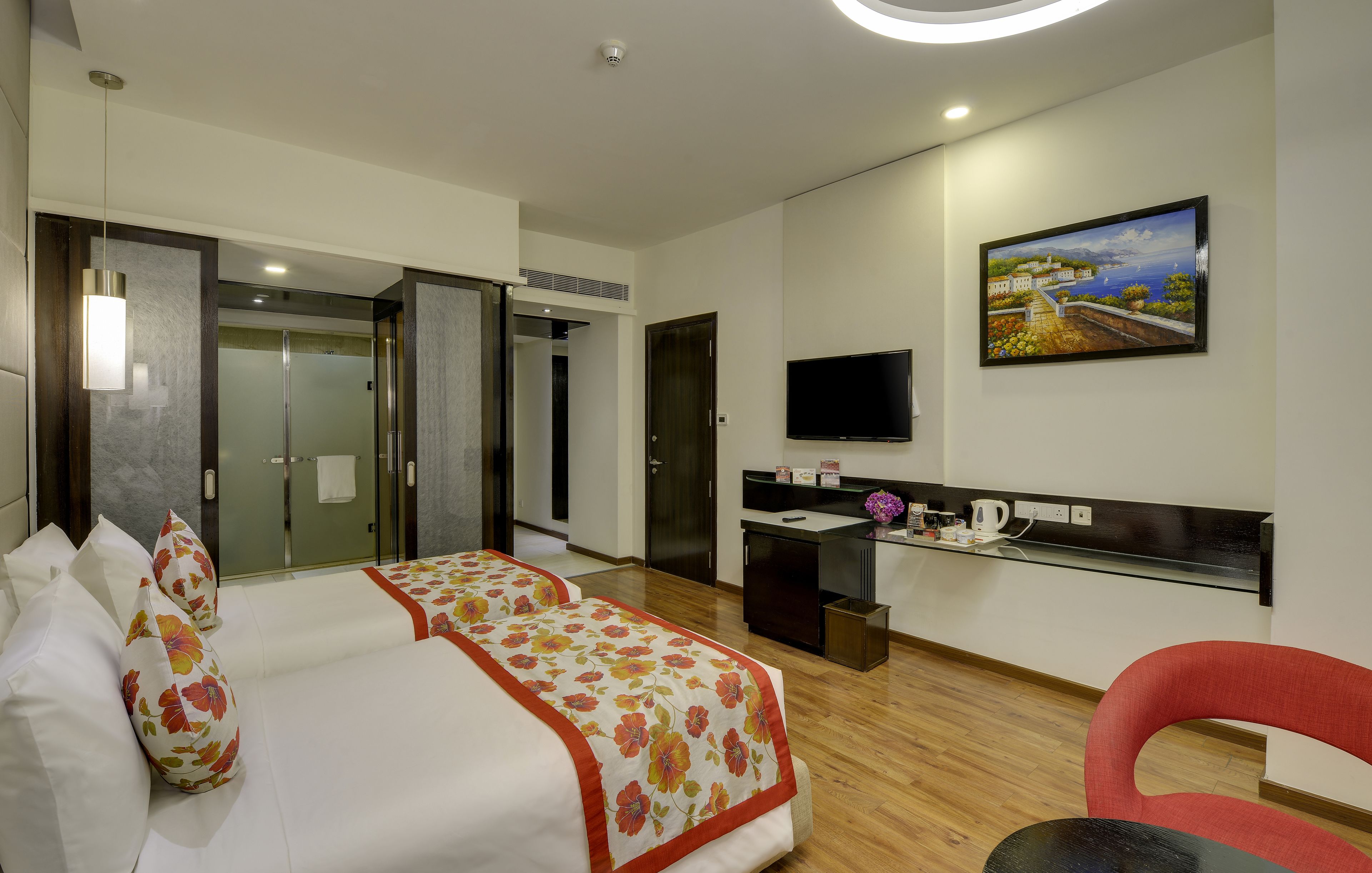 A hotel room with a bed, a desk, a TV, and a painting on the wall.
