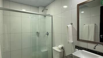 Un baño moderno con ducha de vidrio, inodoro blanco, lavamanos con encimera de granito y espejo con una toalla colgada.