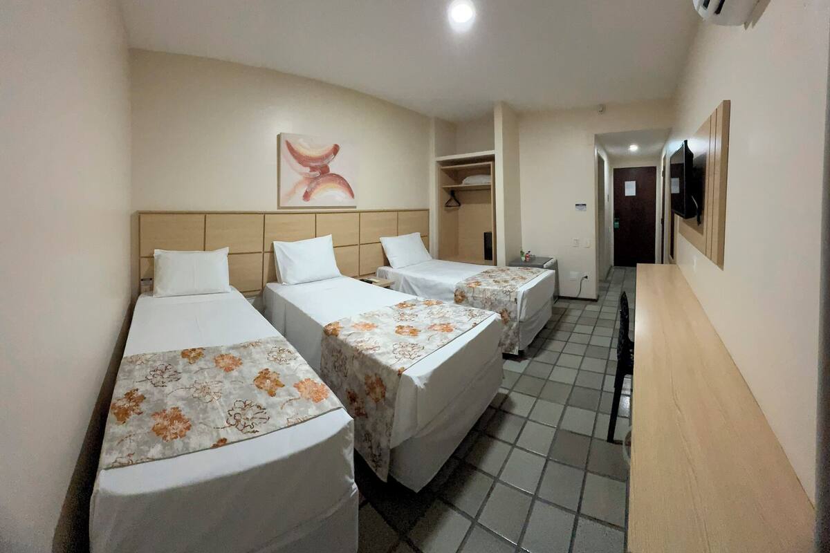 A hotel room with three beds, a small desk, and a TV mounted on the wall.