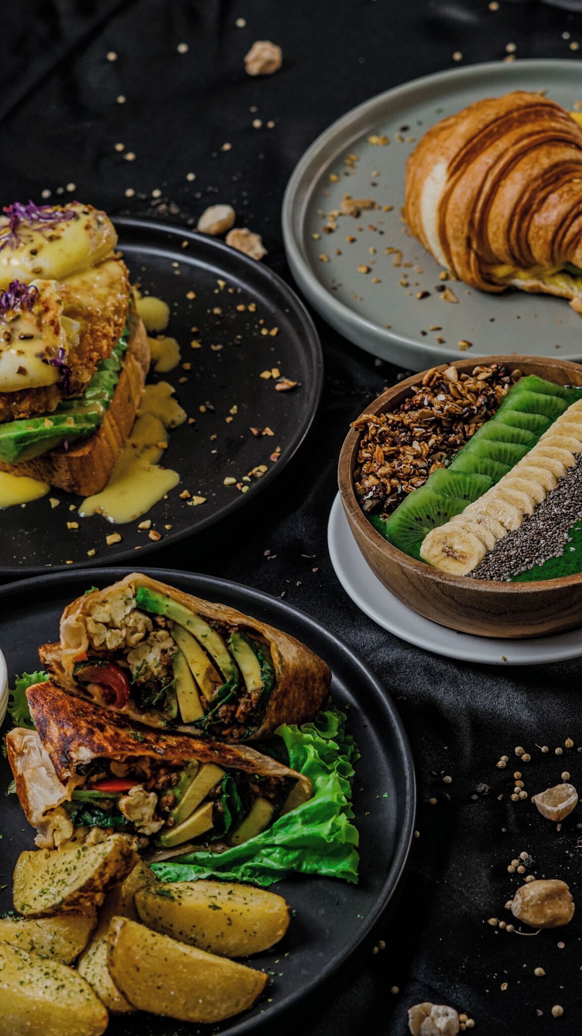 Un assortiment de plats comprenant un sandwich, un croissant et un bol de fruits et de granola.