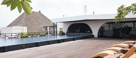 A rooftop pool area with a wooden deck, lounge chairs, and a covered seating area.