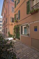 A narrow cobblestone street lined with buildings featuring green shutters and flower boxes.