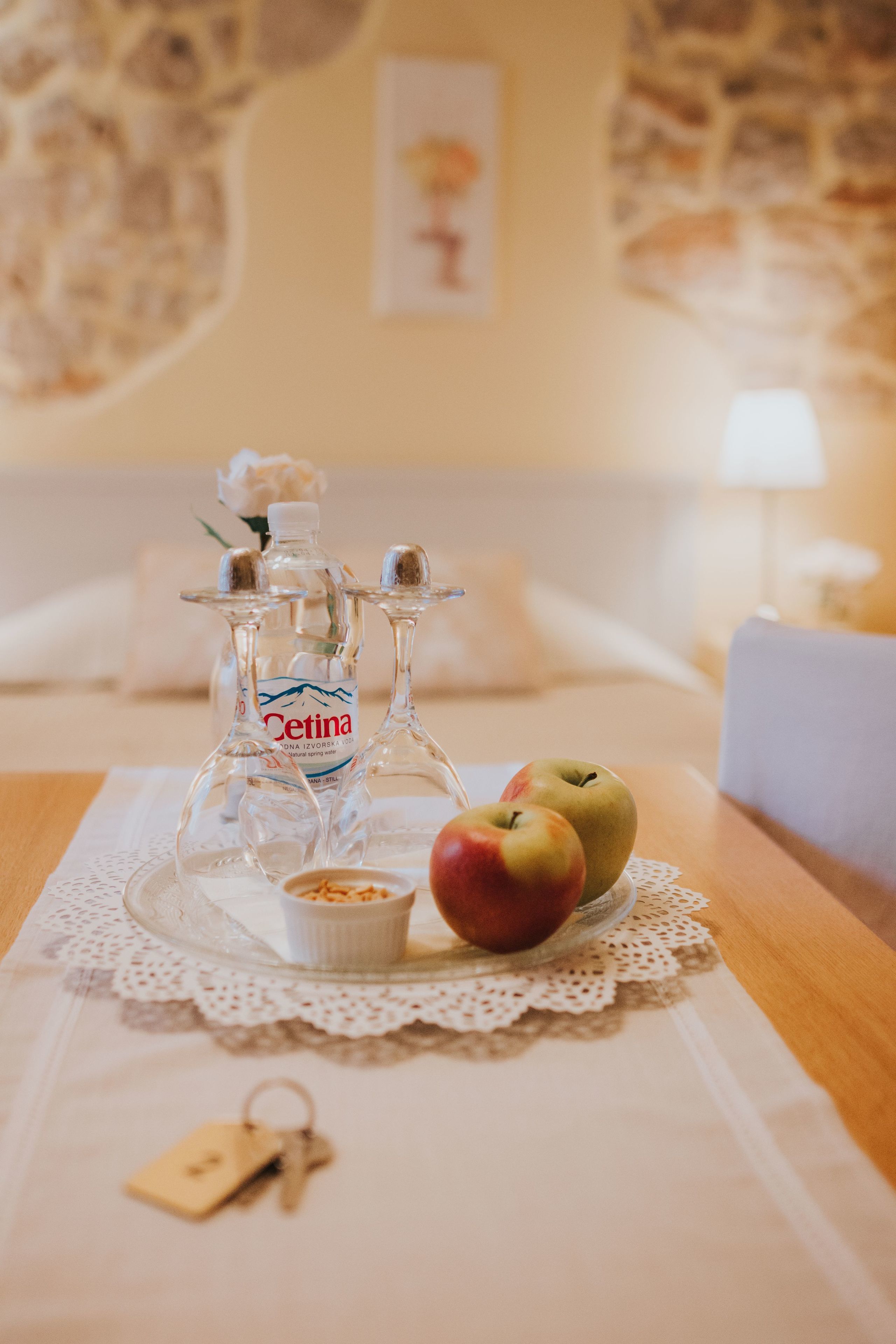 Ett prydligt dukat bord med två flaskor Cetina-vin, en skål med nötter och två äpplen, placerat på en spetsduk.