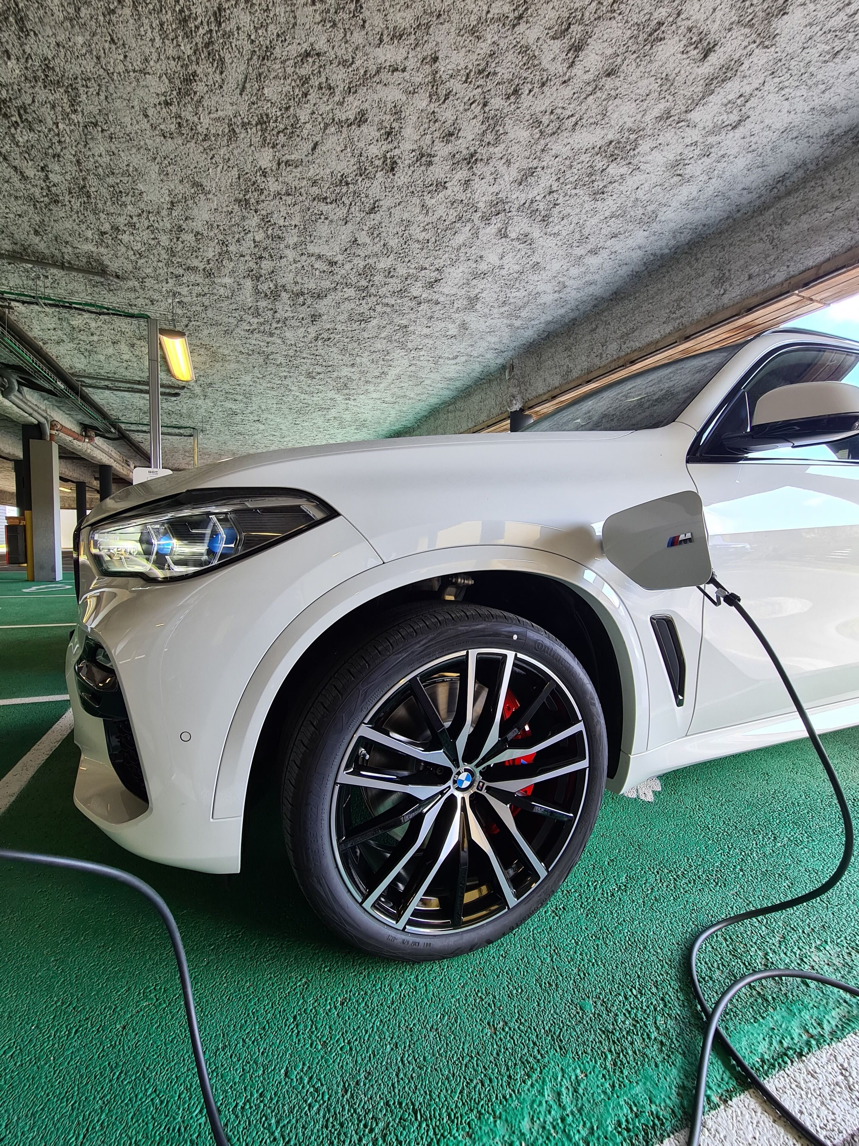 Une voiture blanche est garée dans un garage dont le sol est vert et le plafond présente une texture particulière.