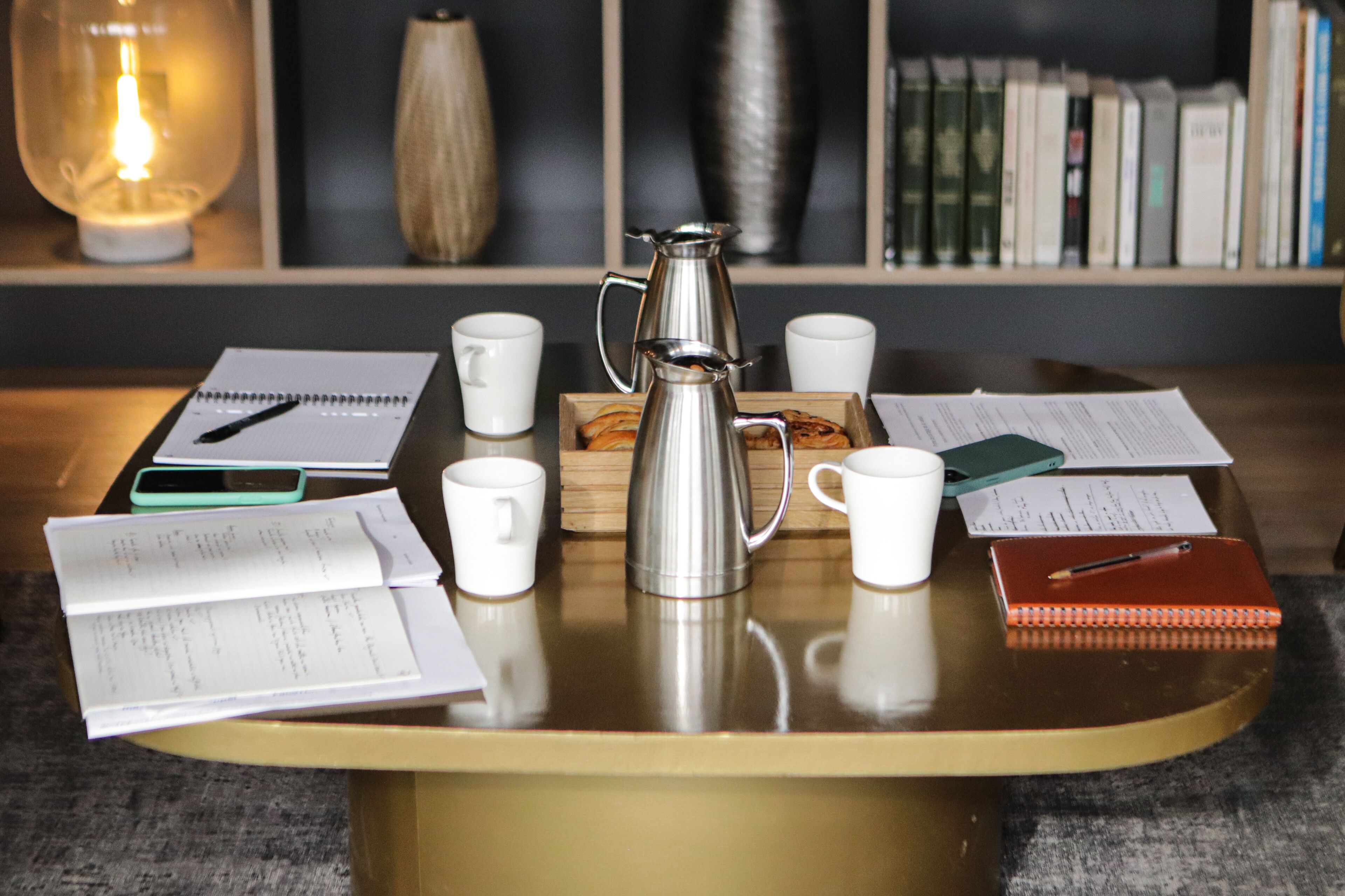 A round table with a coffee pot, notebooks, and papers.