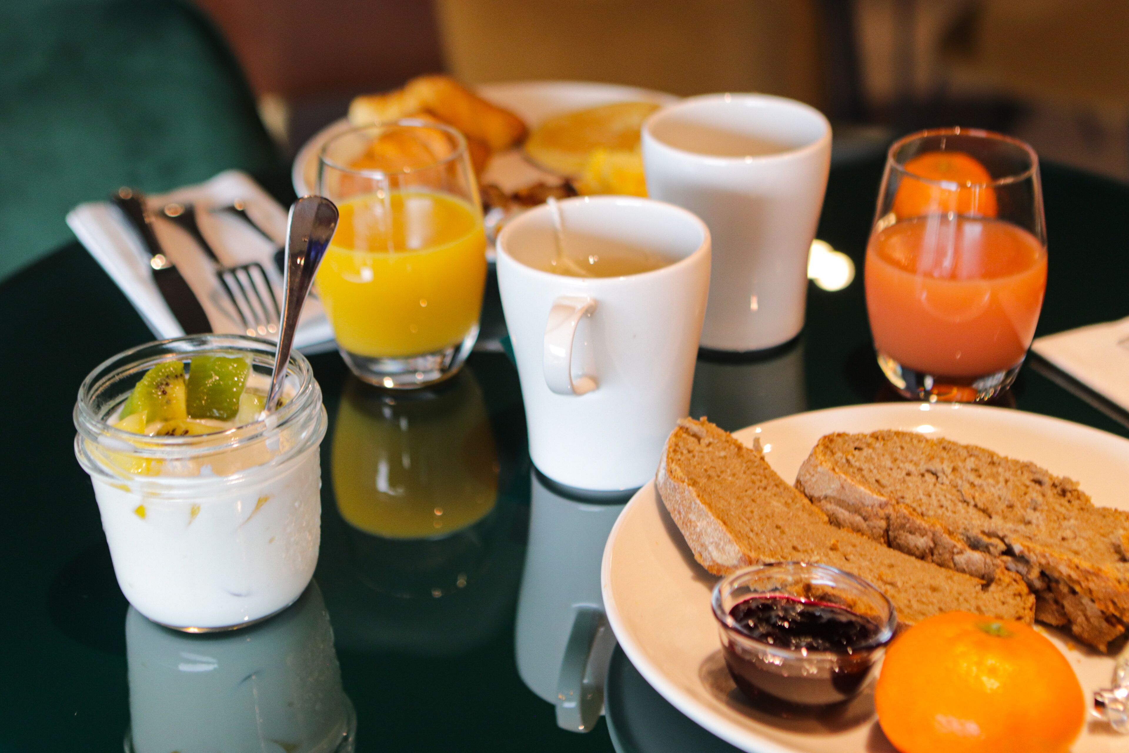 A breakfast setting with a plate of toast, a glass of orange juice, a cup of coffee, and a small jar of yogurt with fruit.