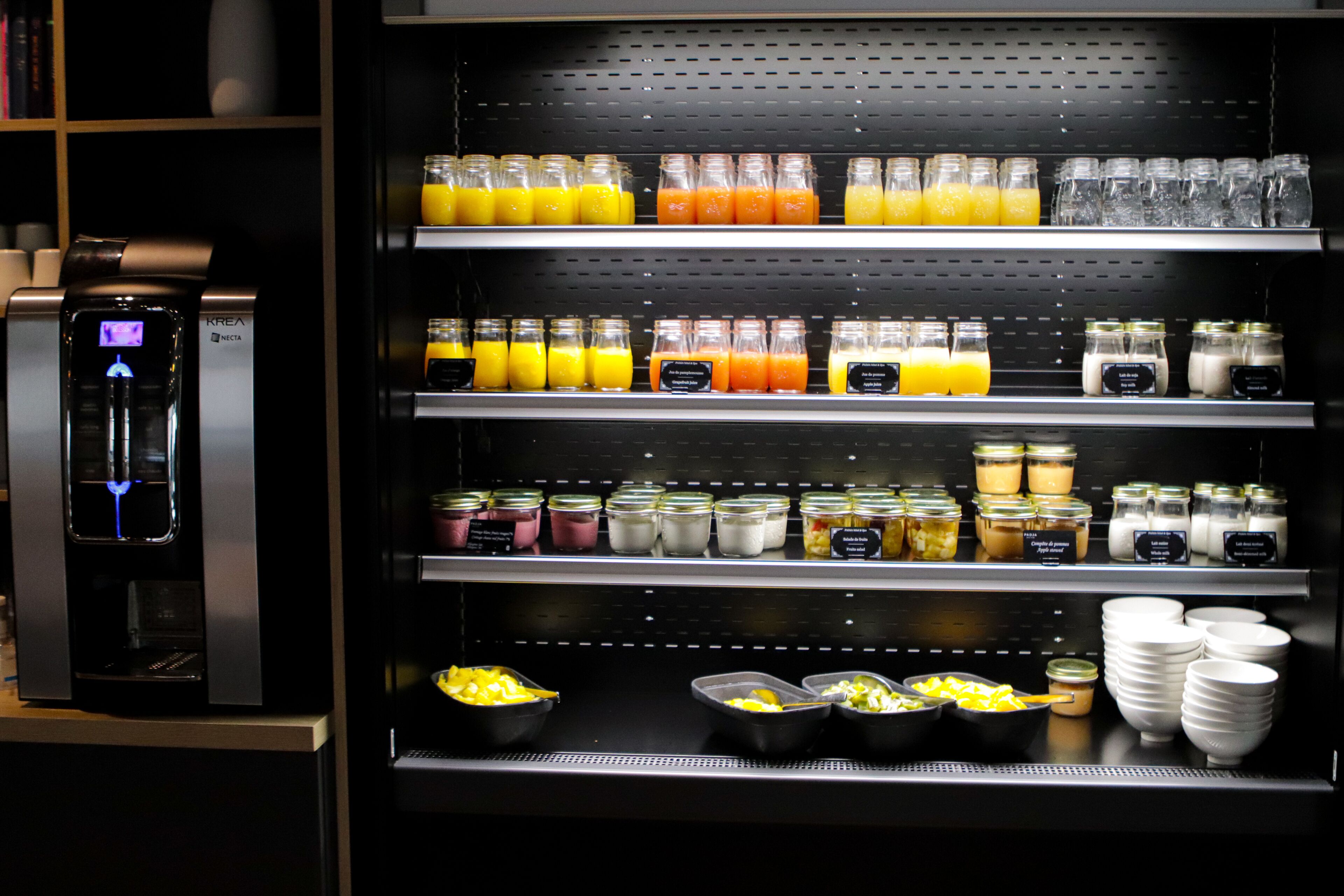 A self-service beverage station with multiple shelves of juices, milk, and yogurt.