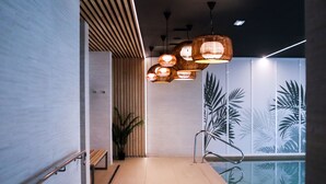 A modern indoor pool area with a wooden bench, a potted plant, and a wall with palm leaf patterns. - Padja Hotel & Spa, Vannes (Vannes)