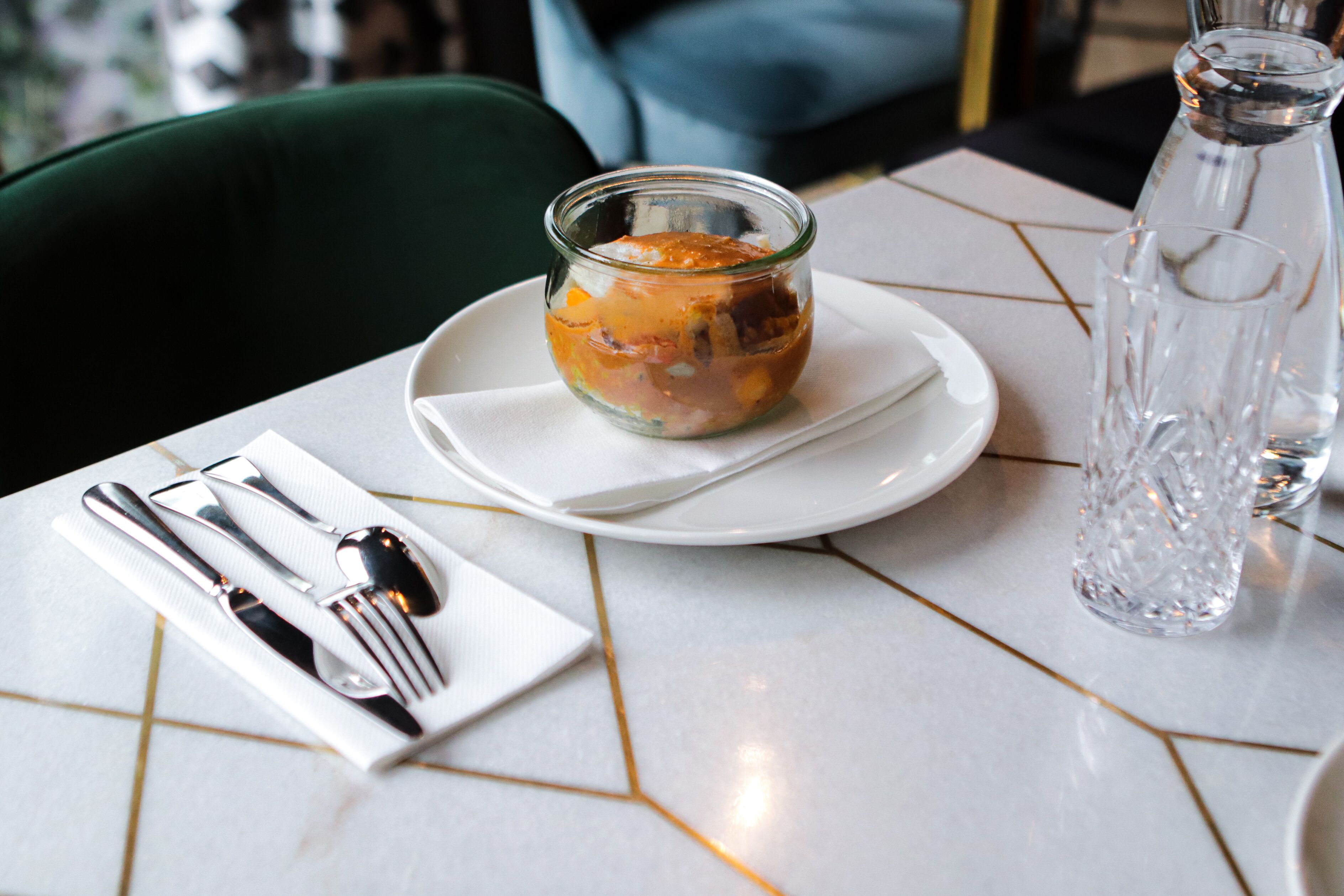 A table with a glass jar of food, a plate, cutlery, and a water bottle.