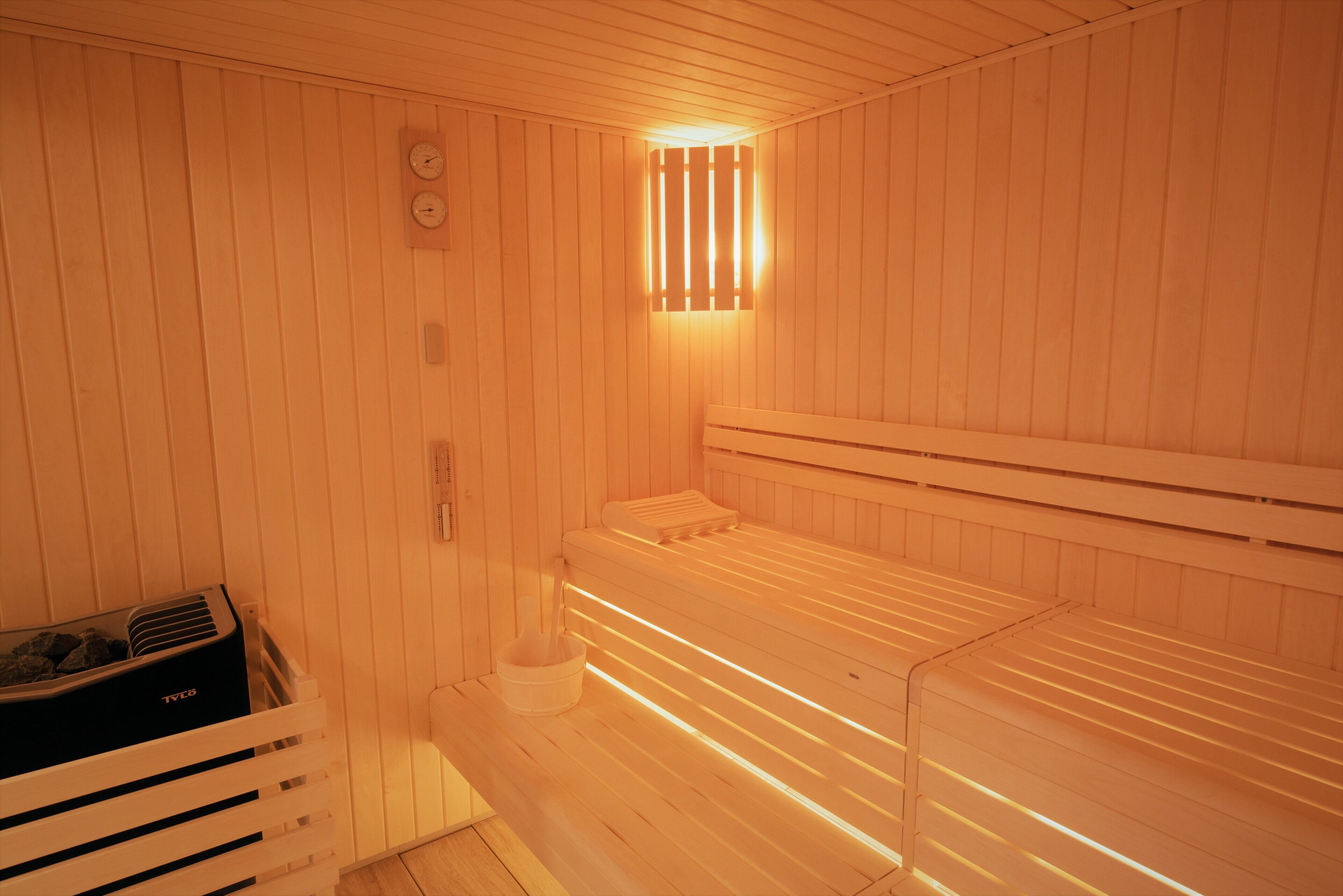 A sauna with wooden walls and benches, a small heater, and a wall-mounted clock.
