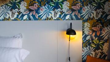Un dormitorio con cama, mesita de noche, lámpara de pared y papel tapiz con estampado floral.