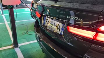 A black BMW 530d parked in a covered parking area with a green floor, charging station, and visible license plate.