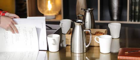 Una mesa con un cuaderno, un bolígrafo, un termo y varias tazas blancas.