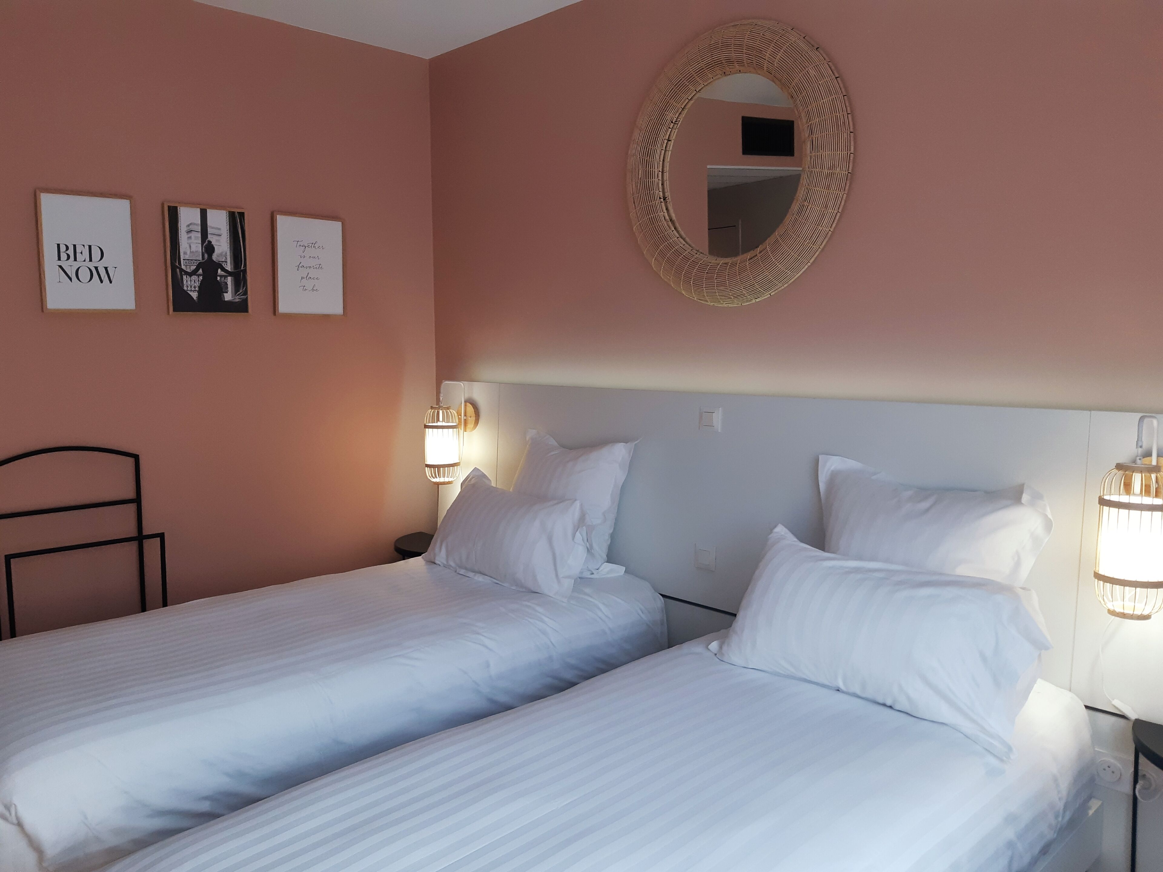 A hotel room with two single beds, a round mirror, and wall-mounted artwork.