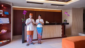 A reception area with a wooden reception desk, a couple standing in front, and a decorative ceiling. - Sense Sunset Hotel Seminyak (Seminyak)