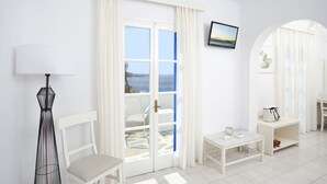 Una habitación luminosa con una silla blanca, una mesita con una taza y un televisor en la pared.