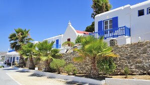 Una calle costera con edificios blancos, contraventanas azules y palmeras.