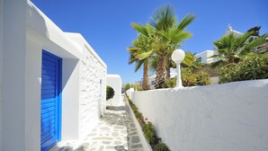 Un callejón estrecho, con paredes blancas, una puerta azul, pavimento de piedra y palmeras.