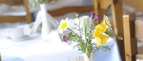 A breakfast table with bread, eggs, ham, butter, coffee, orange juice, and a vase with flowers.