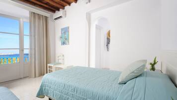 A bedroom with a large bed, a chair, a small table, and a view of the sea through a window.