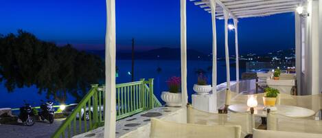 Una terraza con mesas al aire libre, vista al mar y una escalera verde que baja.