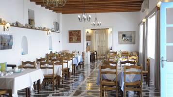 Un restaurant doté de nombreuses tables et chaises, d’un sol carrelé, de poutres en bois au plafond et de lustres.