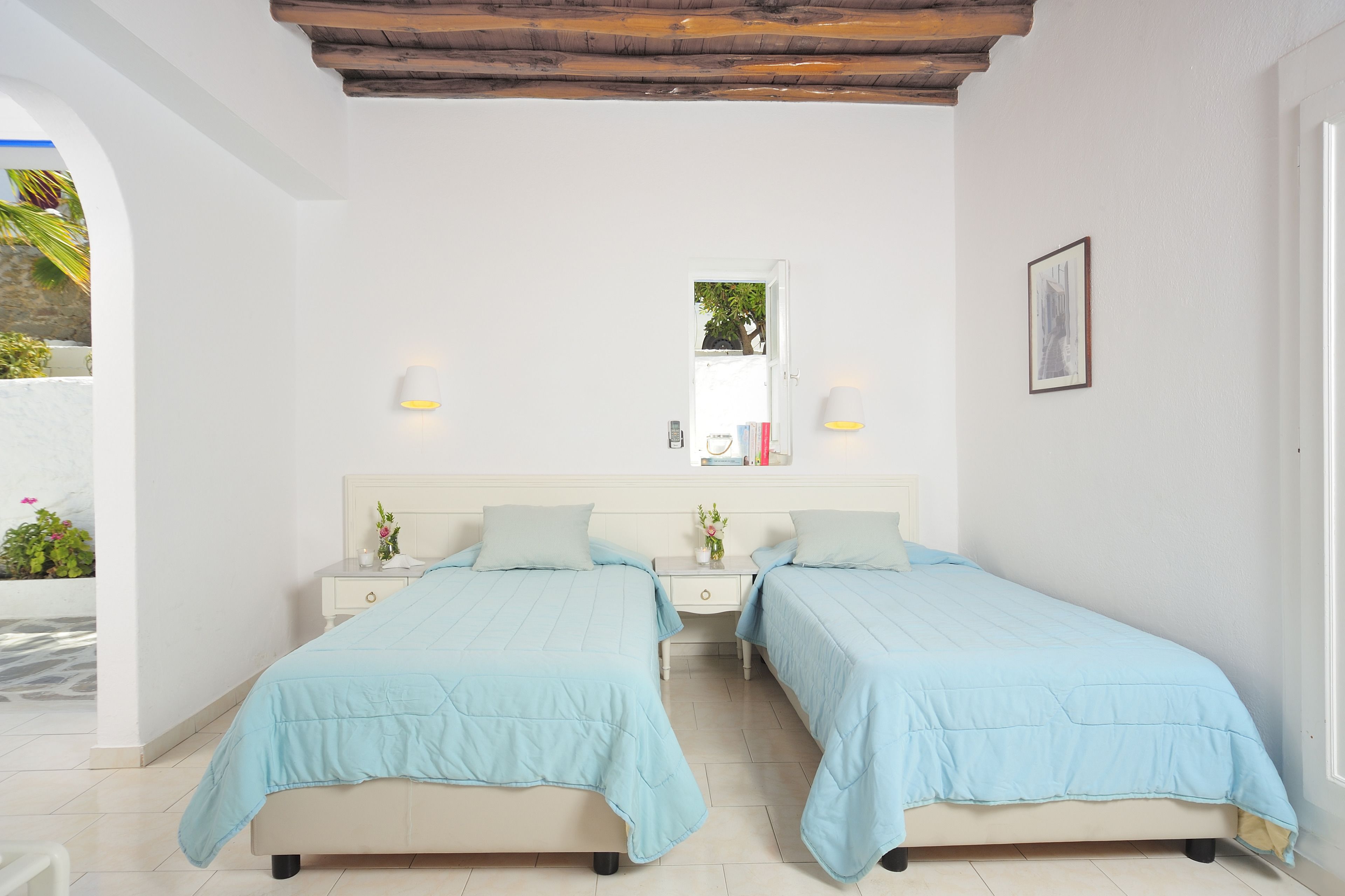 A bedroom with two beds, a nightstand, a mirror, and a door leading to a balcony.