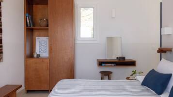 Une chambre à coucher comprenant un lit, une armoire en bois, un petit tabouret, une table de chevet, un miroir et une fenêtre.