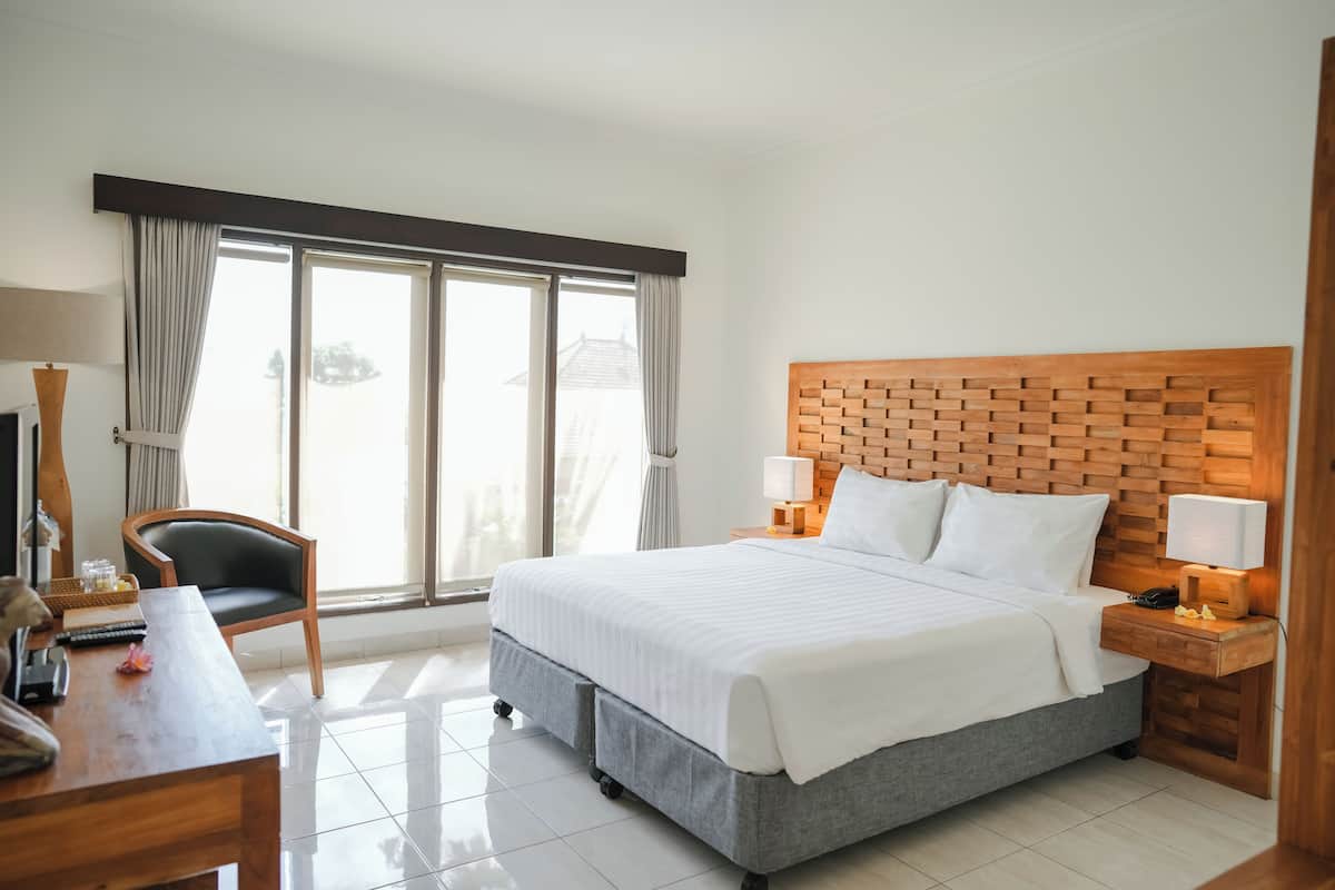 A hotel room with a large bed, a desk, a chair, and a window with curtains.