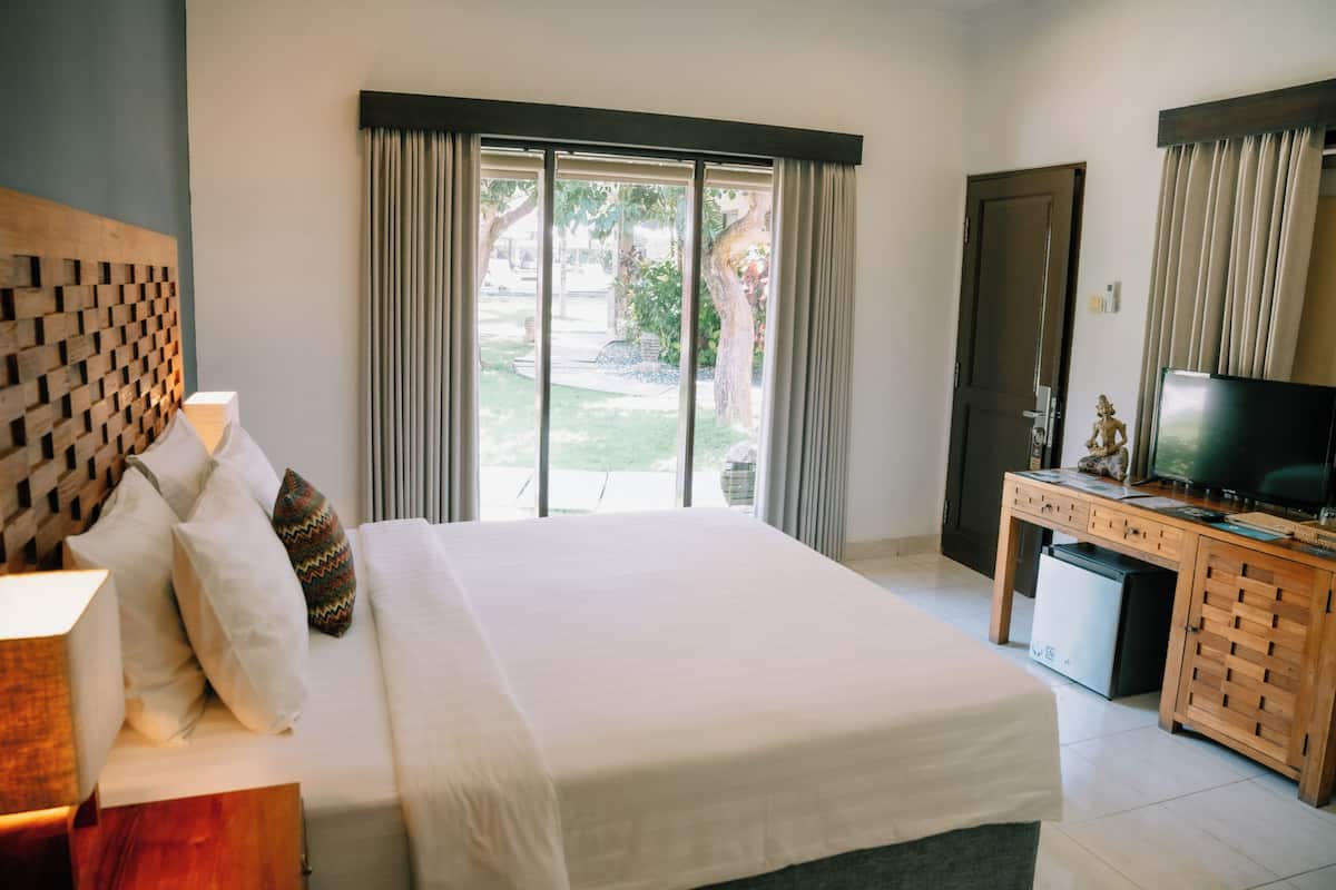 A hotel room with a large bed, a television, a desk, and a view of the outdoors through the window.