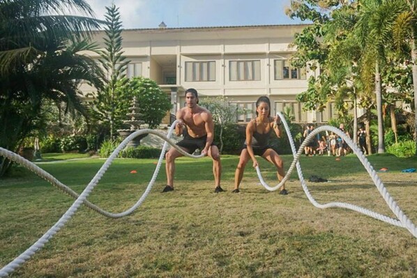 Two people exercising with ropes in a grassy area with a building in the background. - S Resorts Hidden Valley Bali (Pecatu)