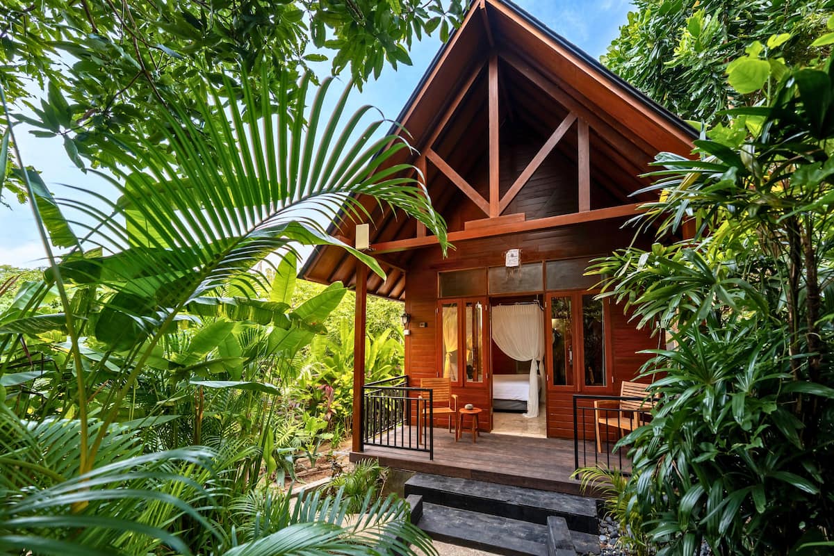 A wooden cabin with a balcony, surrounded by lush greenery.