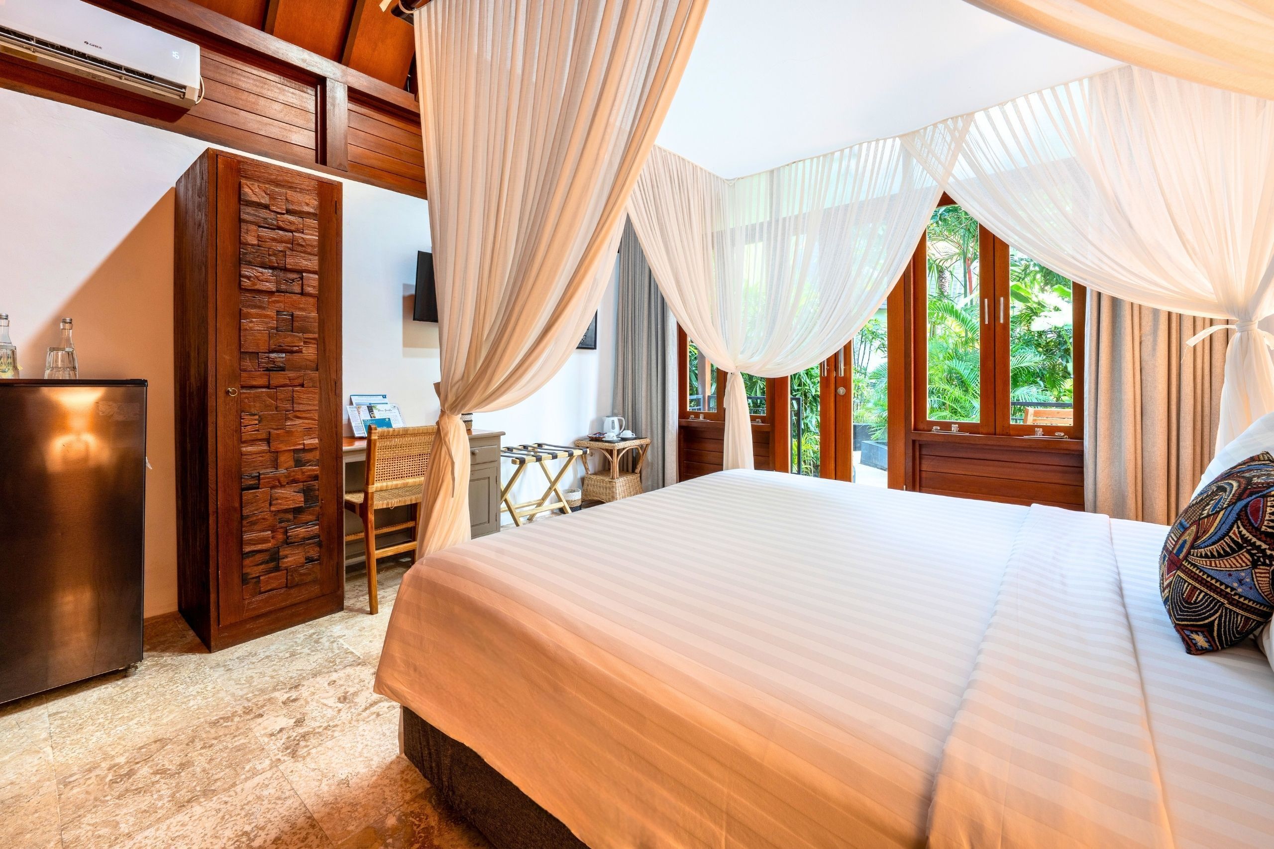 A bedroom with a bed, curtains, a desk, and a view of greenery.