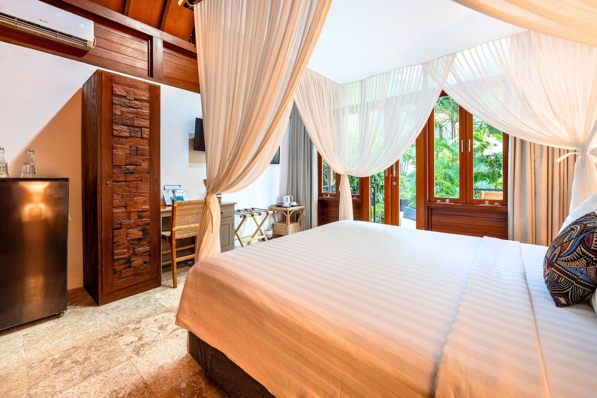 A bedroom with a bed, curtains, a desk, and a view of greenery.