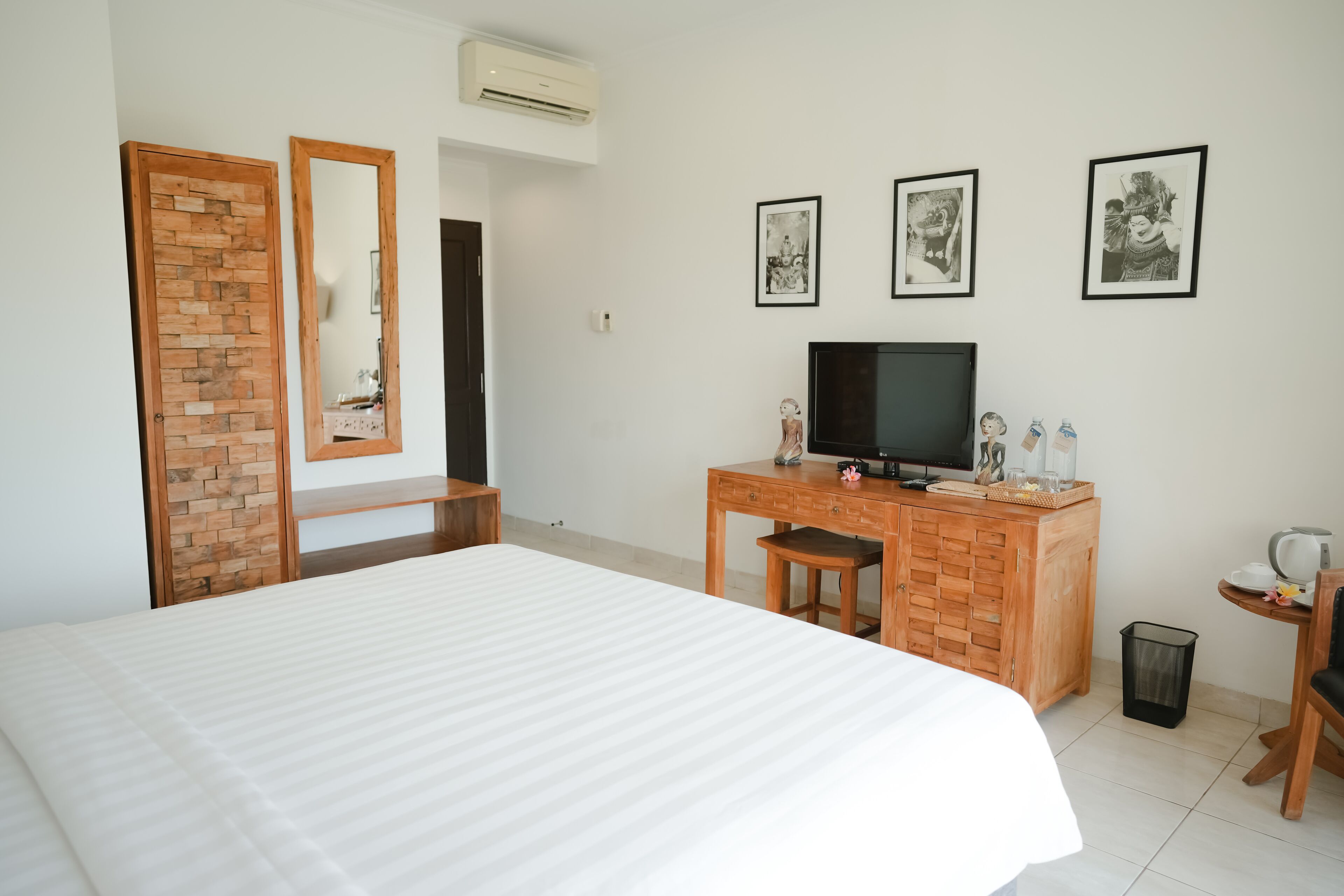 A hotel room with a large bed, a wooden desk with a television, and three framed pictures on the wall.