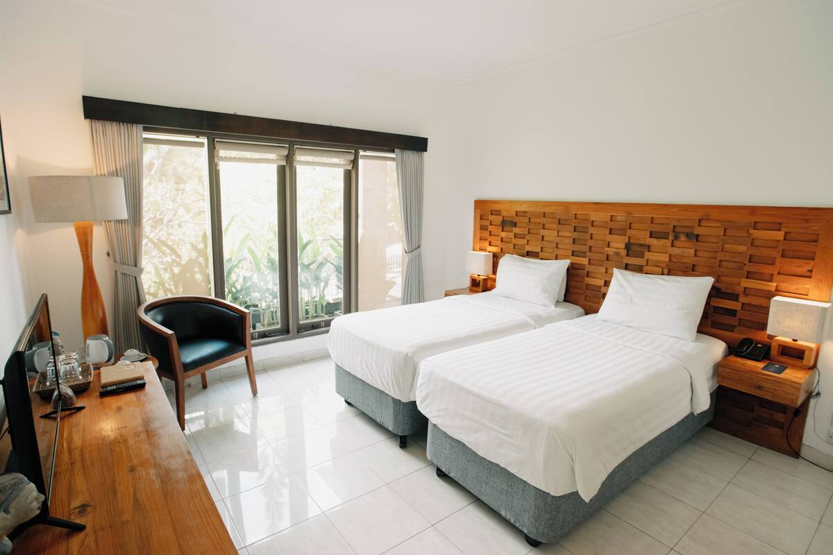 A hotel room with two beds, a desk, a chair, a lamp, and a window with curtains.