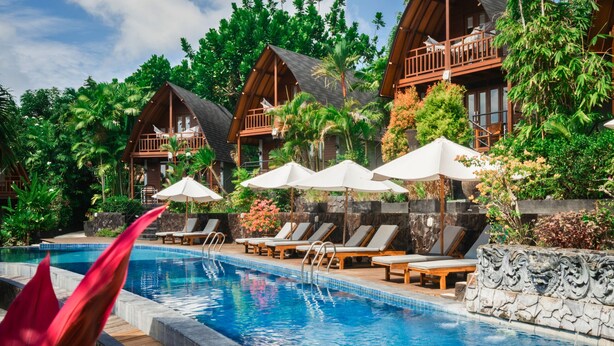 A pool area with lounge chairs and umbrellas, surrounded by wooden cabins and lush greenery. - S Resorts Hidden Valley Bali (Pecatu)