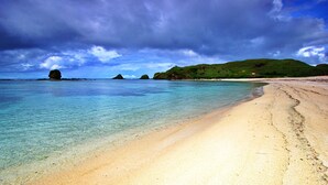 A beach with clear turquoise water, sandy shore, and green hills in the background. - S Resorts Hidden Valley Bali (Pecatu)