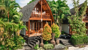 A wooden cabin with a balcony, surrounded by lush greenery and palm trees. - S Resorts Hidden Valley Bali (Pecatu)