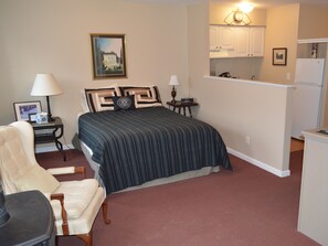 A bedroom with a bed, a chair, a nightstand, a lamp, a picture frame, and a painting on the wall.