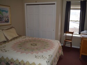 A bedroom with a bed, a chair, a desk, and a window with curtains.