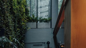 An indoor seating area with a sofa, chairs, and a table, surrounded by greenery and a brick wall.