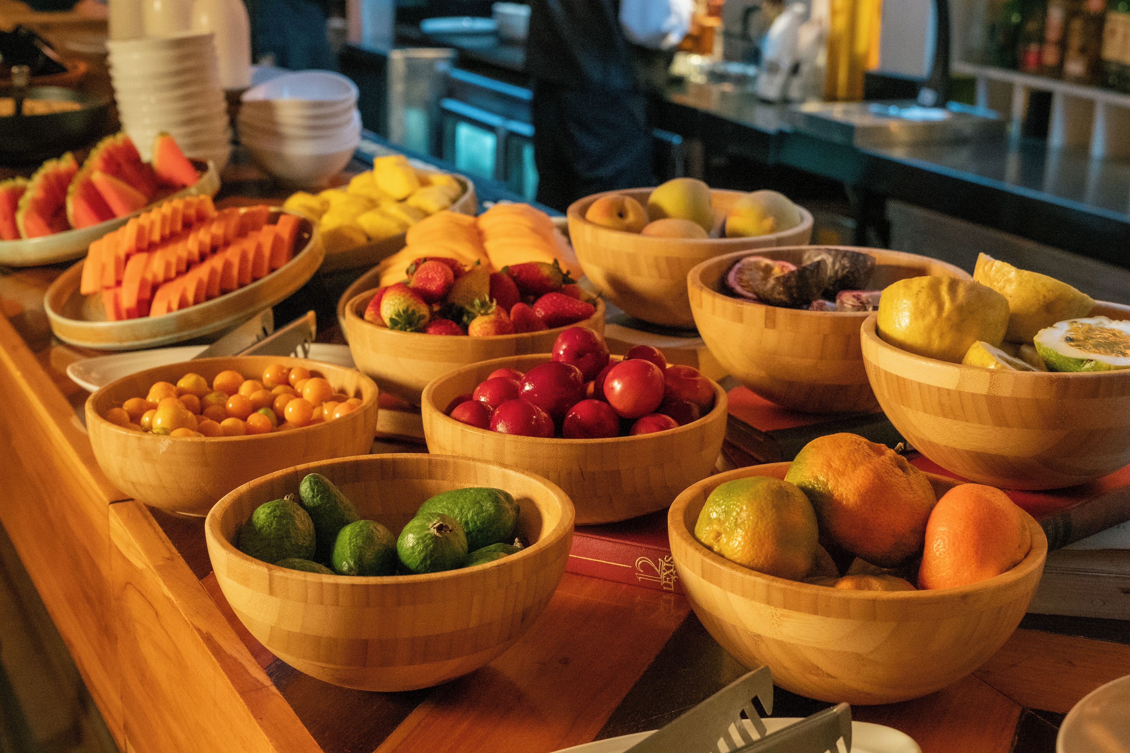 A buffet table with various wooden bowls filled with fruits and vegetables.