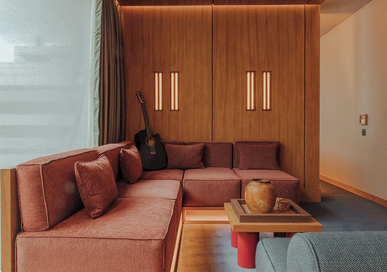 Un salon moderne avec un canapé d’angle, un meuble en bois doté de panneaux rétroéclairés, une guitare et une petite table en bois agrémentée d’objets décoratifs.