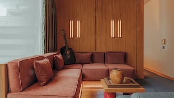 Un salon moderne avec un canapé d’angle, un meuble en bois doté de panneaux rétroéclairés, une guitare et une petite table en bois agrémentée d’objets décoratifs.